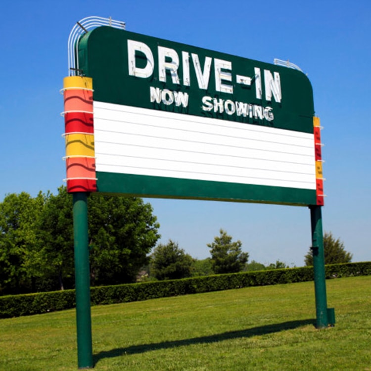 drive-in sign on a grassy lawn with trees and a blue sky in the background